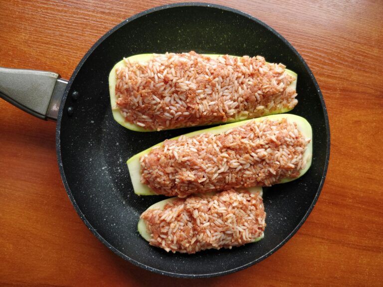 Appetizing stuffed zucchini with rice, served in a skillet on a wooden table.