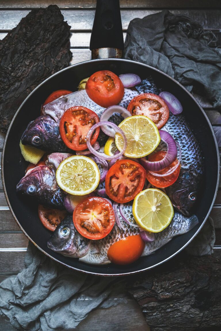 Colorful arrangement of fresh fish with lemon and tomato slices in a pan, ready for cooking.