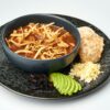 Bowl of rich tortilla soup served with avocado slices, grated cheese, and bread.